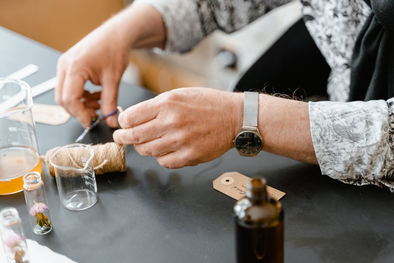 Hands crafting scents with natural ingredients and glass bottles on a table.
